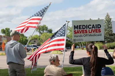 Residents hold American flags and a "Medicaid Saves Lives" sign at the Good Trouble rally in Brookings, South Dakota.